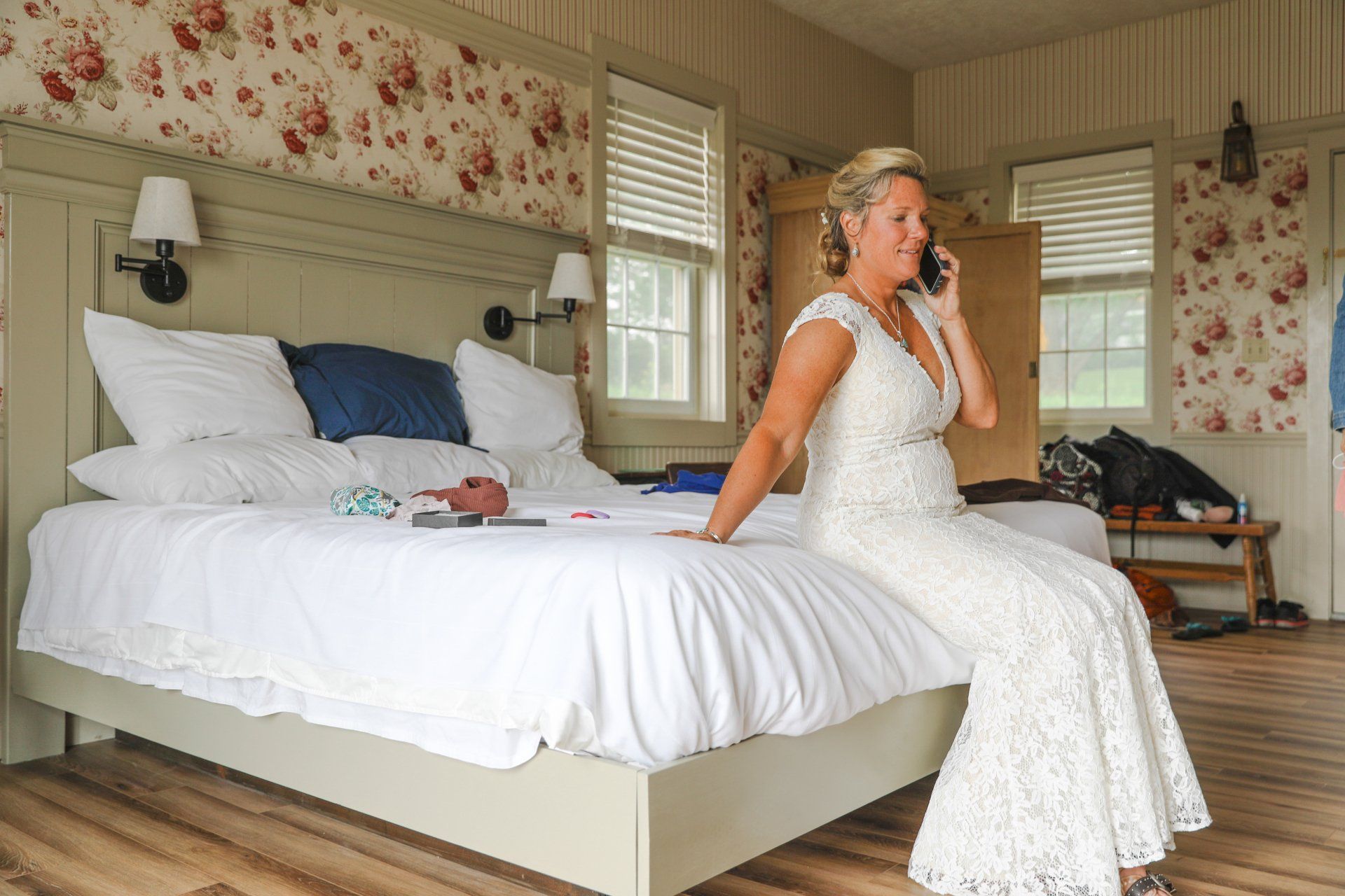 Woman in a white dress sitting on a bed in a floral bedroom, talking on a phone