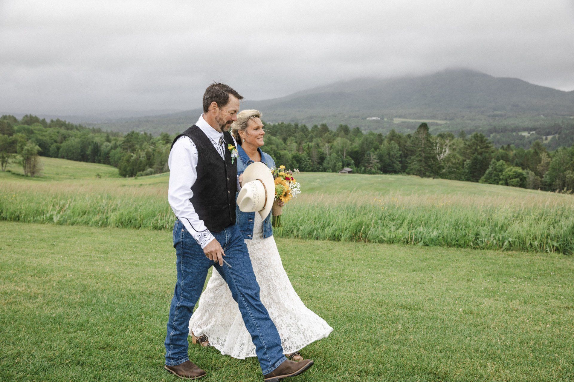 Couple walking in a grassy field with mountains in the background on a cloudy day