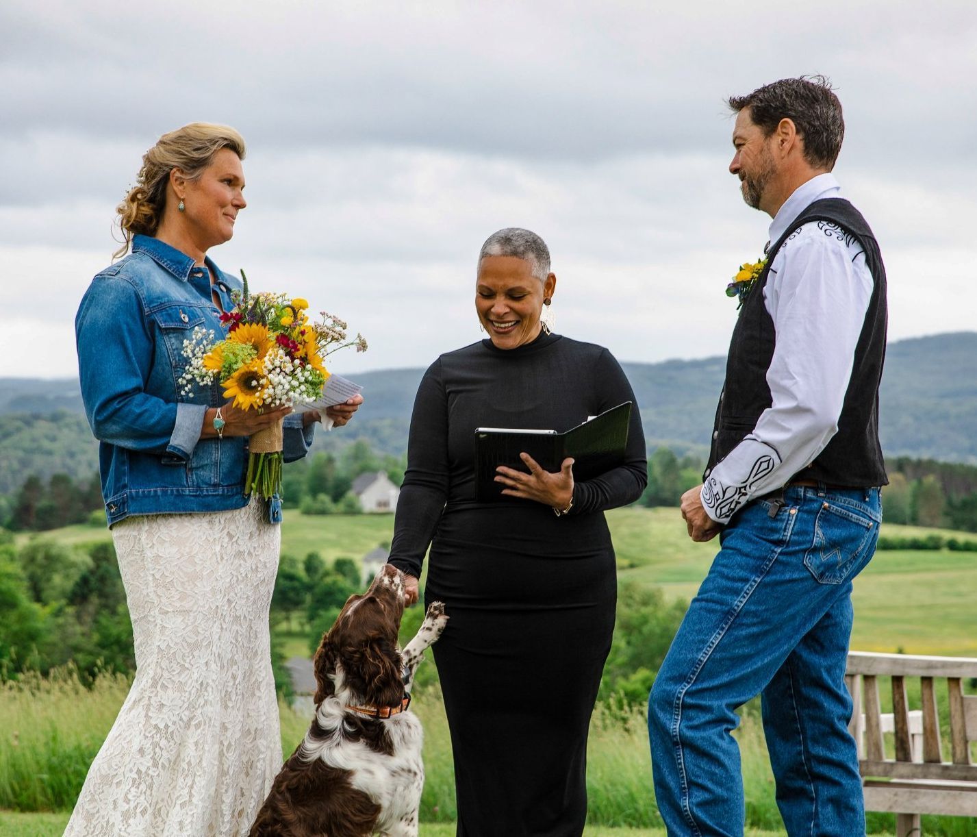 Three people and a dog outdoors, one holding flowers and another reading from a card.
