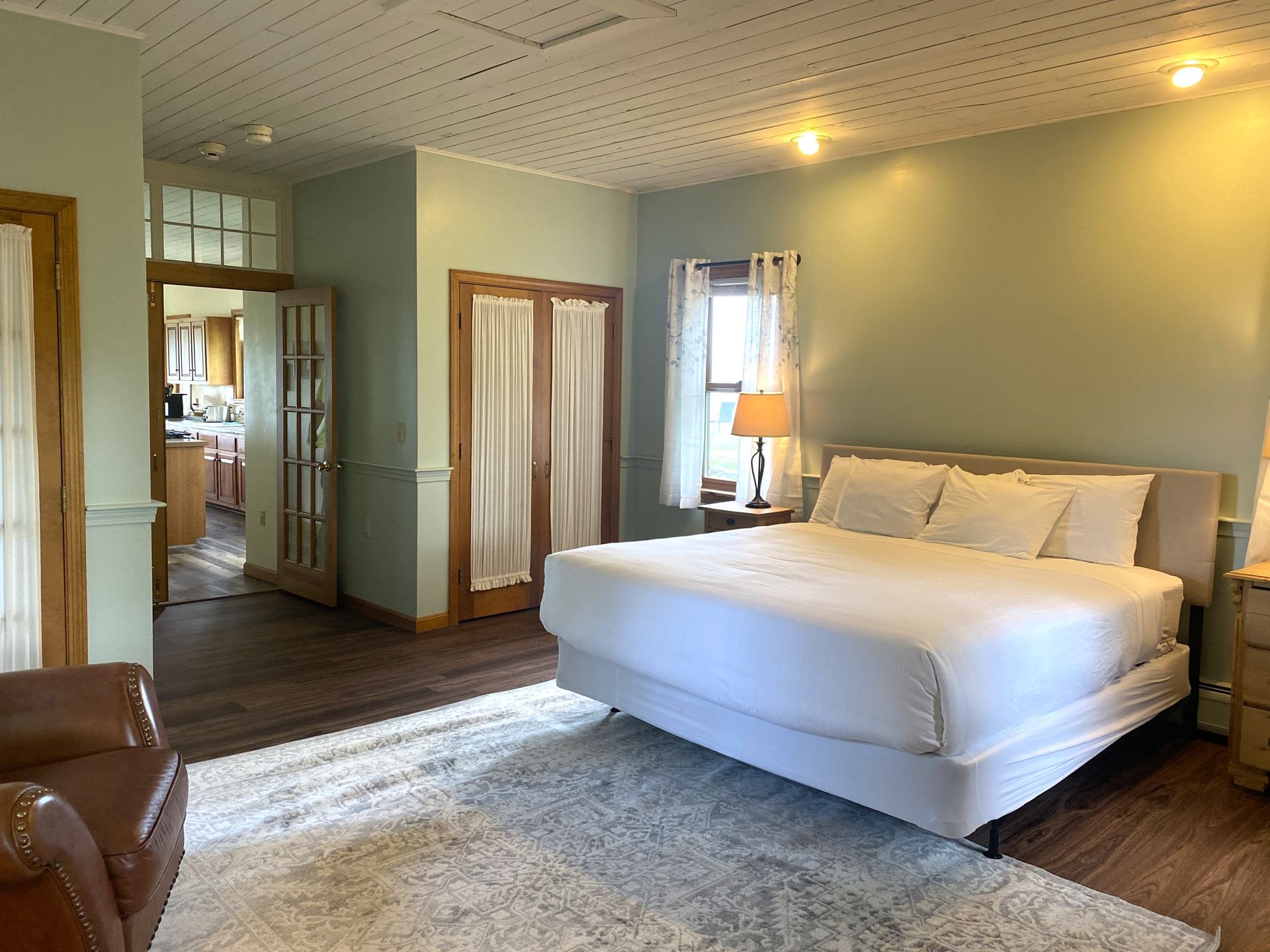 Bright bedroom with a large white bed, soft green walls, dark wood floors, and a floor lamp.