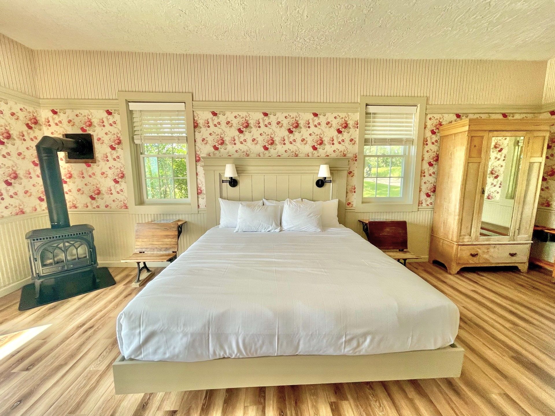 Cozy bedroom with a white bed, wood stove, patterned wallpaper, and large wardrobe on hardwood floors