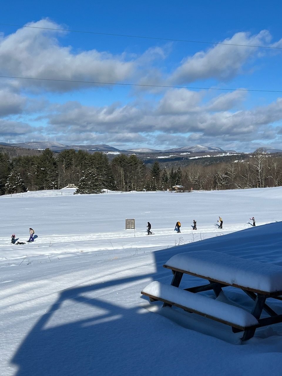 Snowshoers and cross-country skiers crossing the Wildflower Inn's snowy field on a bluebird morning in Lyndonville, Vermont
