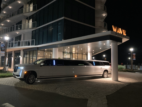 A white stretch limousine parked under the lighted entrance of the Wave Resort at night.