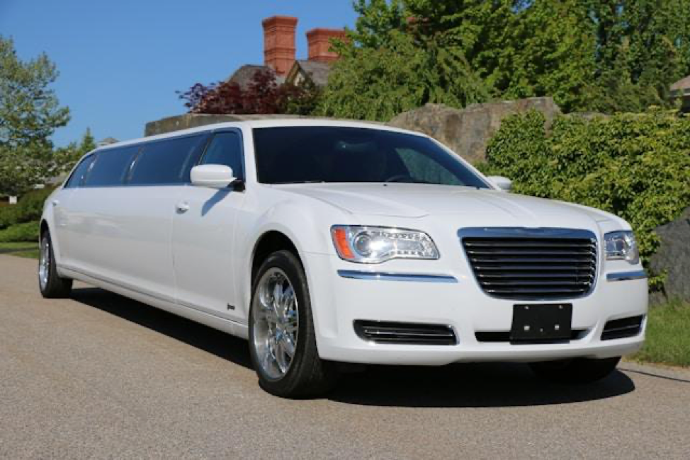 A white Chrysler 300 stretch limousine parked on an asphalt driveway during the day.