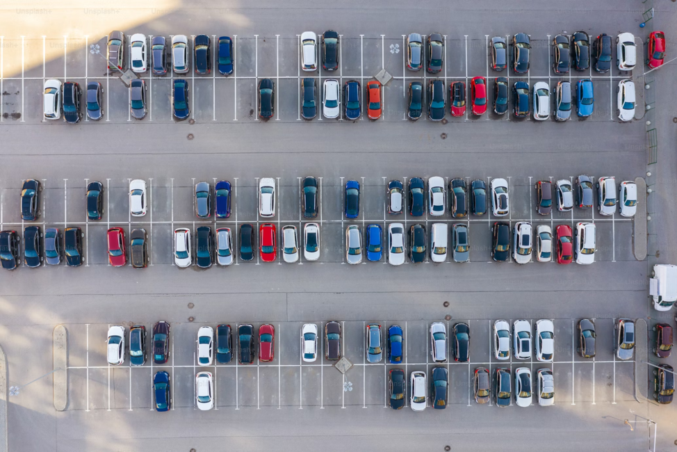 An aerial view of a parking lot filled with many cars of various colors parked in orderly rows.
