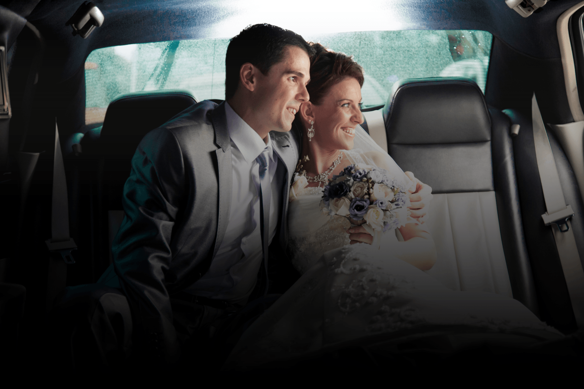 A smiling bride and groom sitting together in the back seat of a car.