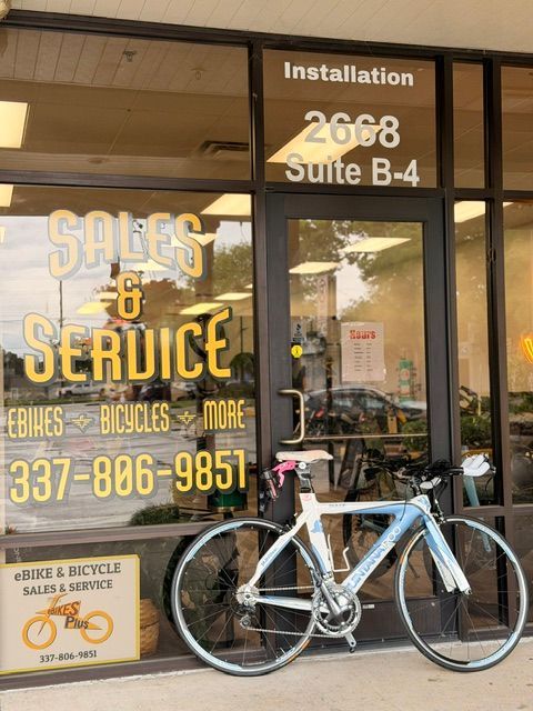 Blue bicycle parked outside a sales and service bike shop with orange signage and glass storefront