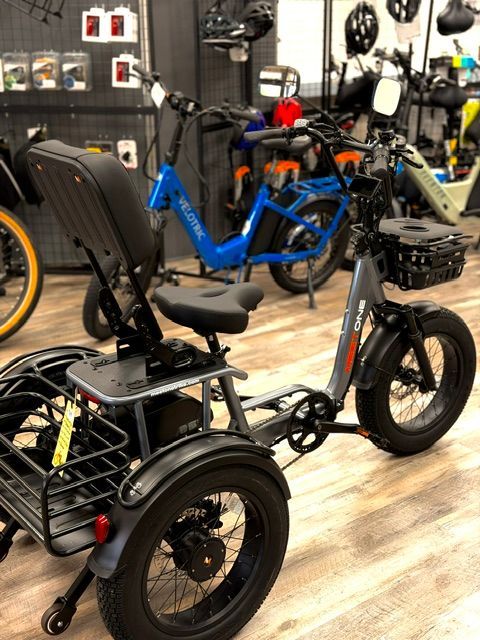 Three-wheeled black and blue cargo bike in a bike shop with electric bikes in the background