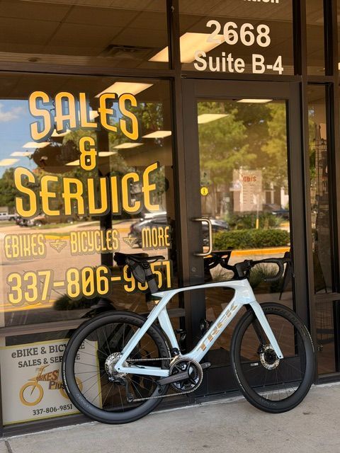 White road bicycle parked outside a Sales & Service bike shop with glass door and window signage