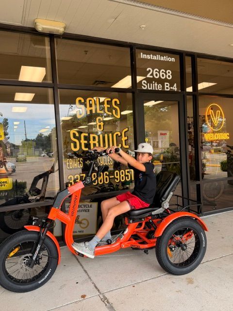 Person on orange motorbike outside storefront with “Sales & Service” sign and glass door.