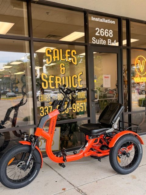 Orange three-wheeled electric trike parked outside a sales and service shop.