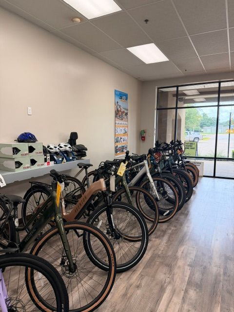 Indoor bicycle shop with several bikes lined up on a wood floor near a glass entrance.