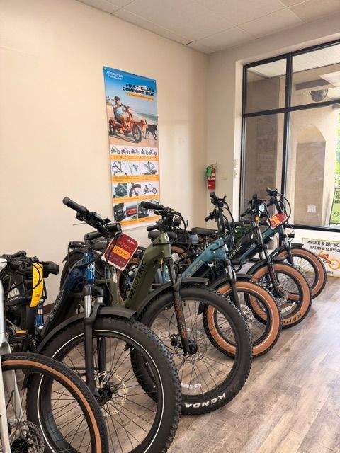 Row of fat-tire e-bikes parked indoors beside a wall poster and glass door