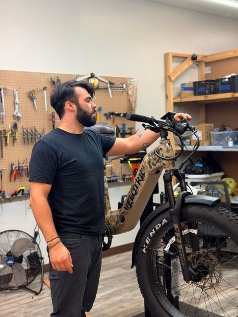 Man in a black shirt inspecting a beige electric bike in a workshop