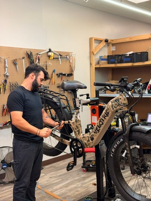 Man working on a camo mountain bike in a workshop with tools on the wall