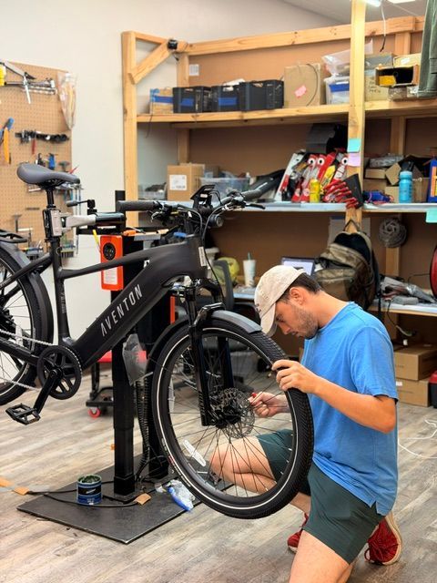 Person kneeling beside a black bicycle on a repair stand in a workshop, fixing the front wheel