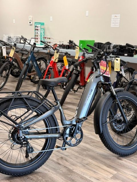 Row of electric bikes in a showroom, with a gray bike in the foreground and colorful bikes behind.