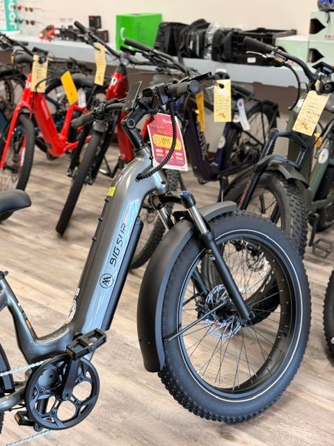 Electric bikes lined up in a showroom, with a gray fat-tire e-bike in the foreground.