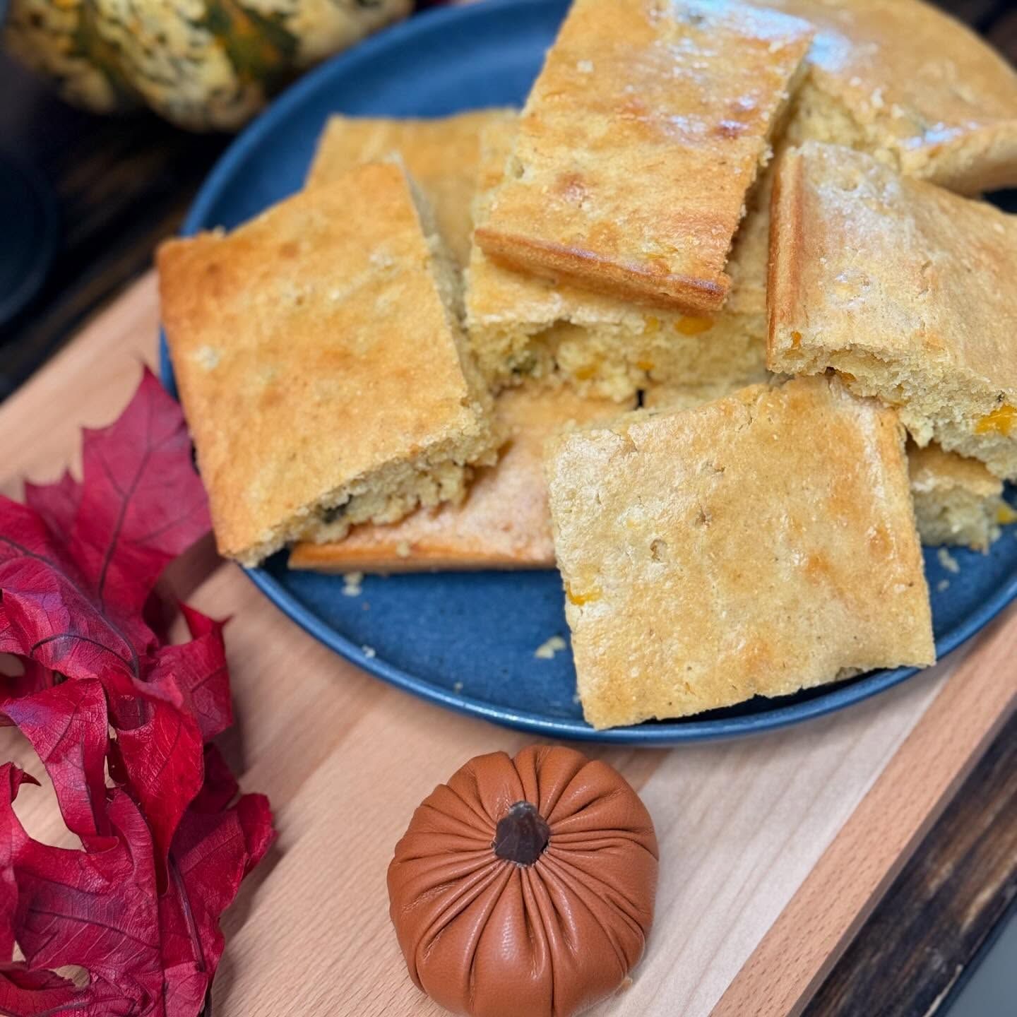 Square golden cake pieces on a blue plate with a red leaf and a small carved pumpkin decoration