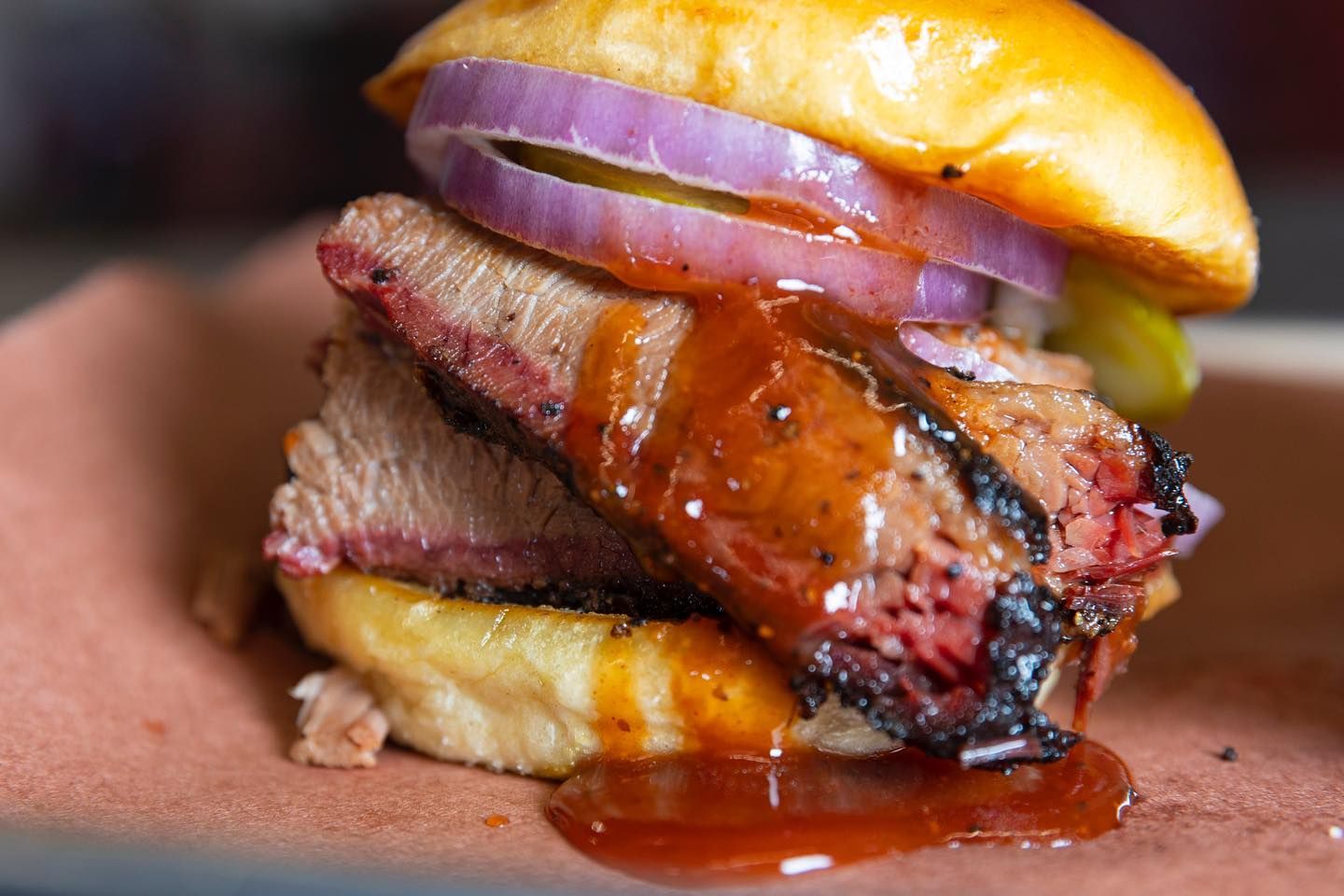 Close-up of a juicy cheeseburger with red onion and sauce dripping on a plate