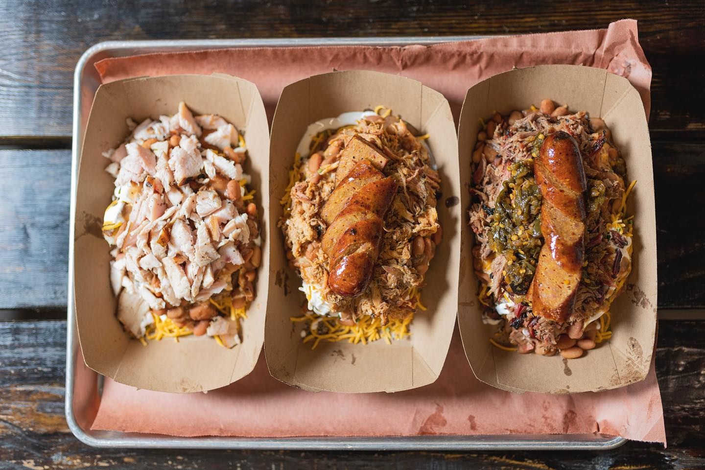 Three tacos on a tray, one topped with white sauce, one with melted cheese, and one with salsa and herbs.