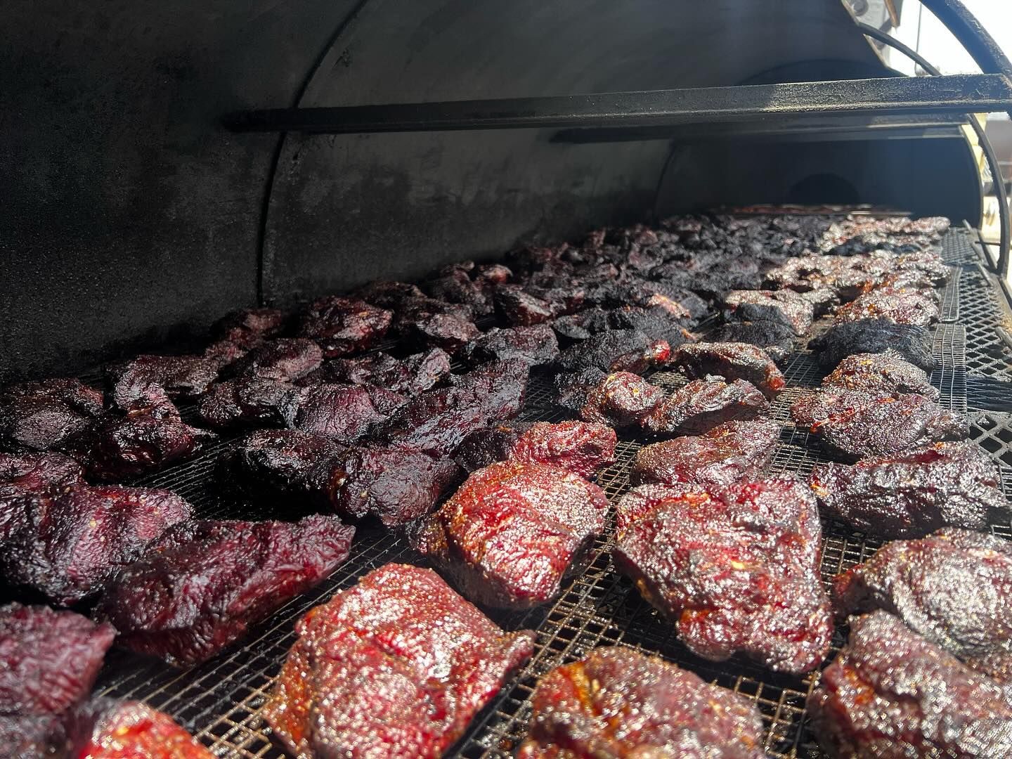 Smoked meat cooking on a grill, with dark charred pieces over glowing coals