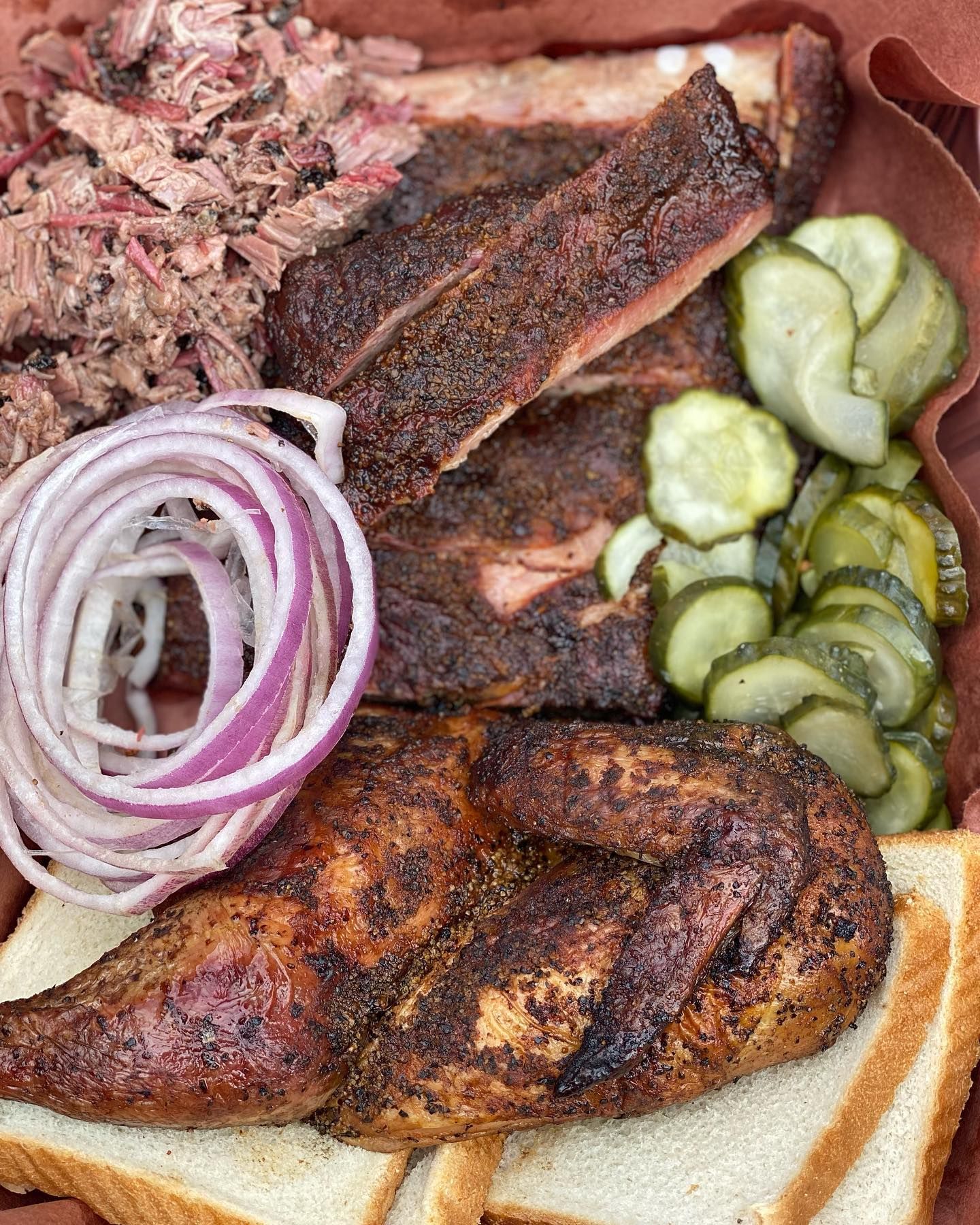 Plate of smoked meat with pickles, red onion, and bread on a wooden tray