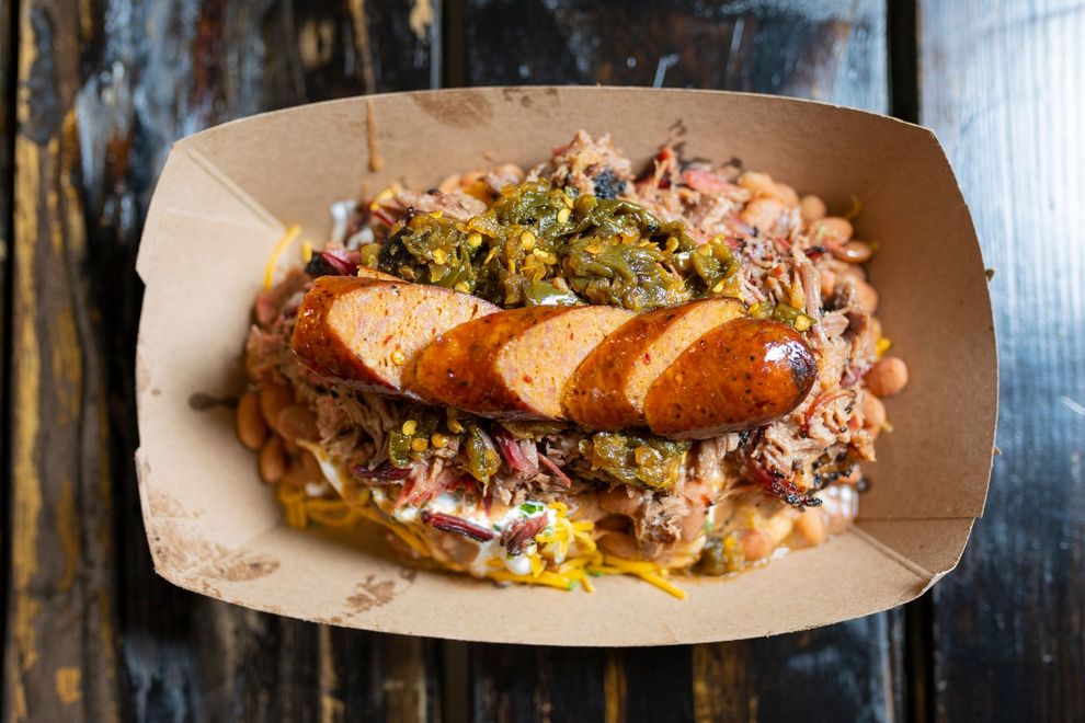 Sliced sausage over sauerkraut in a cardboard takeout tray on a rustic wooden table