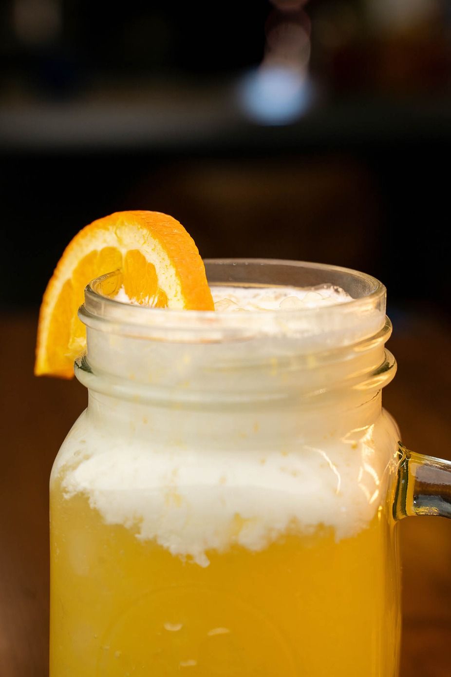 Mason jar of orange cocktail with ice and an orange slice garnish