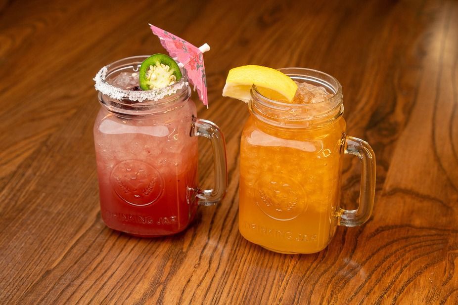 Two colorful mason jar cocktails with fruit garnishes on a wooden table