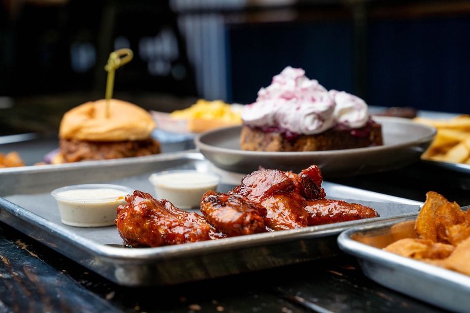 Assorted barbecue dishes on metal trays, including glazed ribs, a burger, fries, and a dessert on a table