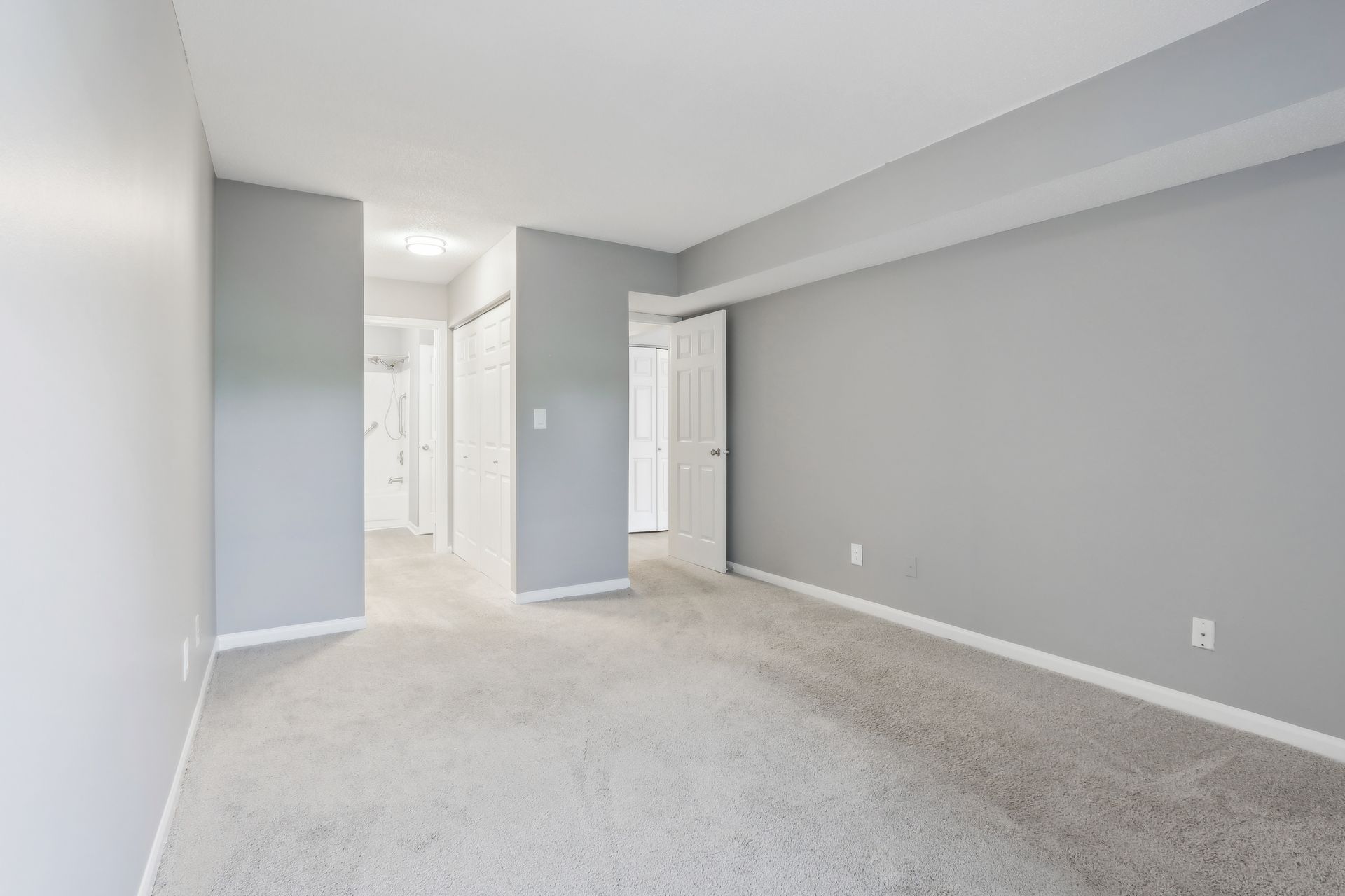 Empty bedroom with gray walls and carpet, doorways lead to hallways.