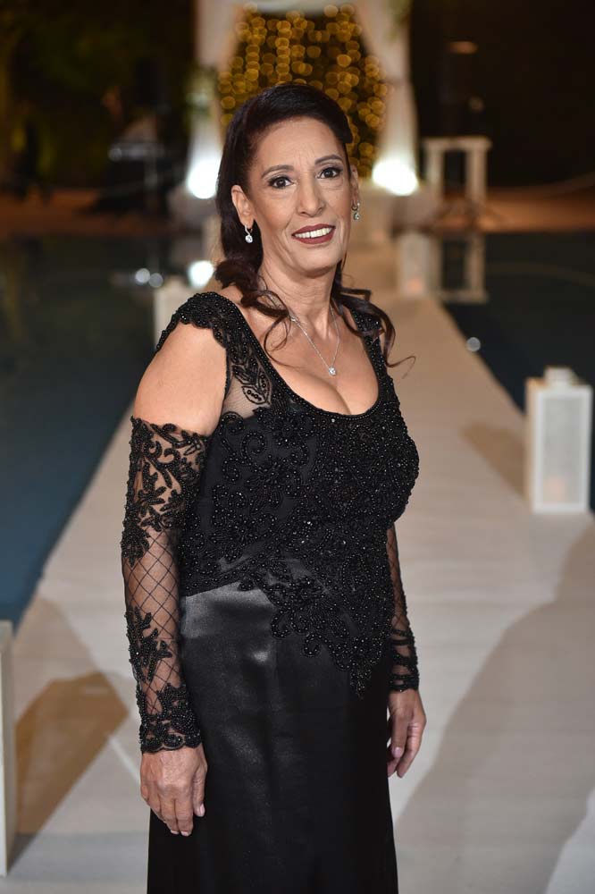 אישה בשמלת חרוזים שחורה מחייכת בחוץ, ליד בריכה ועיצוב חתונה.
