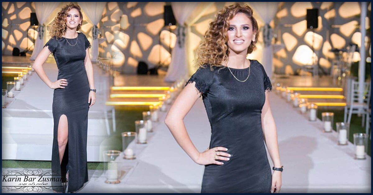אישה בשמלה שחורה מצטלמת על מסלול לבן; התפאורה היא אירוע עם אורות ונרות.