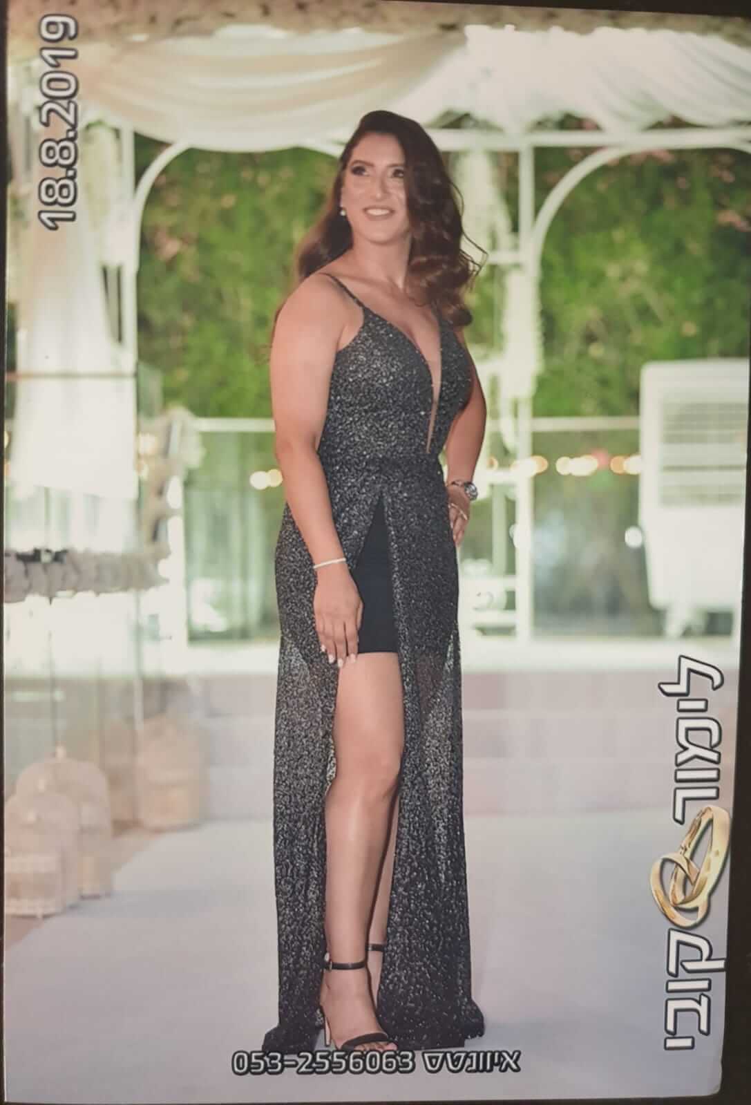 אישה בשמלה שחורה נוצצת עם שס בגובה הירכיים, מצטלמת בחוץ על פלטפורמה לבנה.