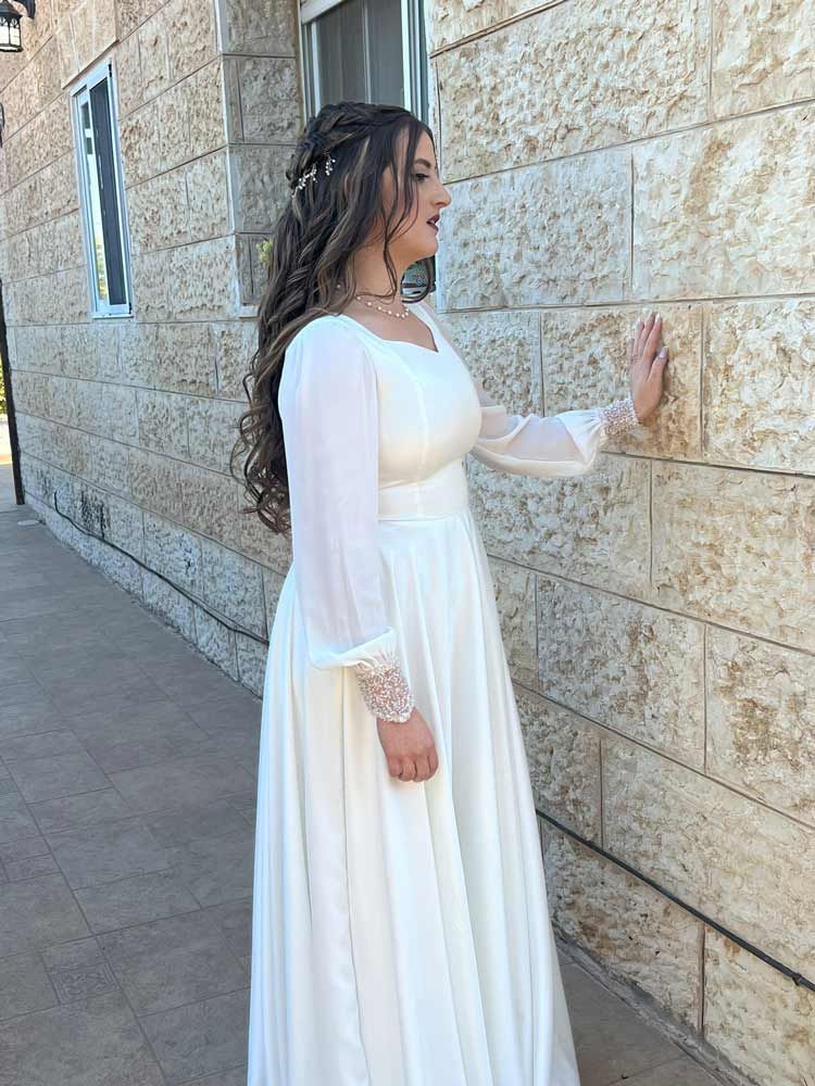 אישה בשמלה לבנה נוגעת בקיר אבן בחוץ.