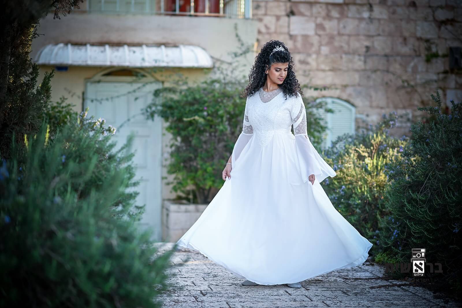אישה צעירה בשמלה לבנה, נוף גן, מצטלמת.