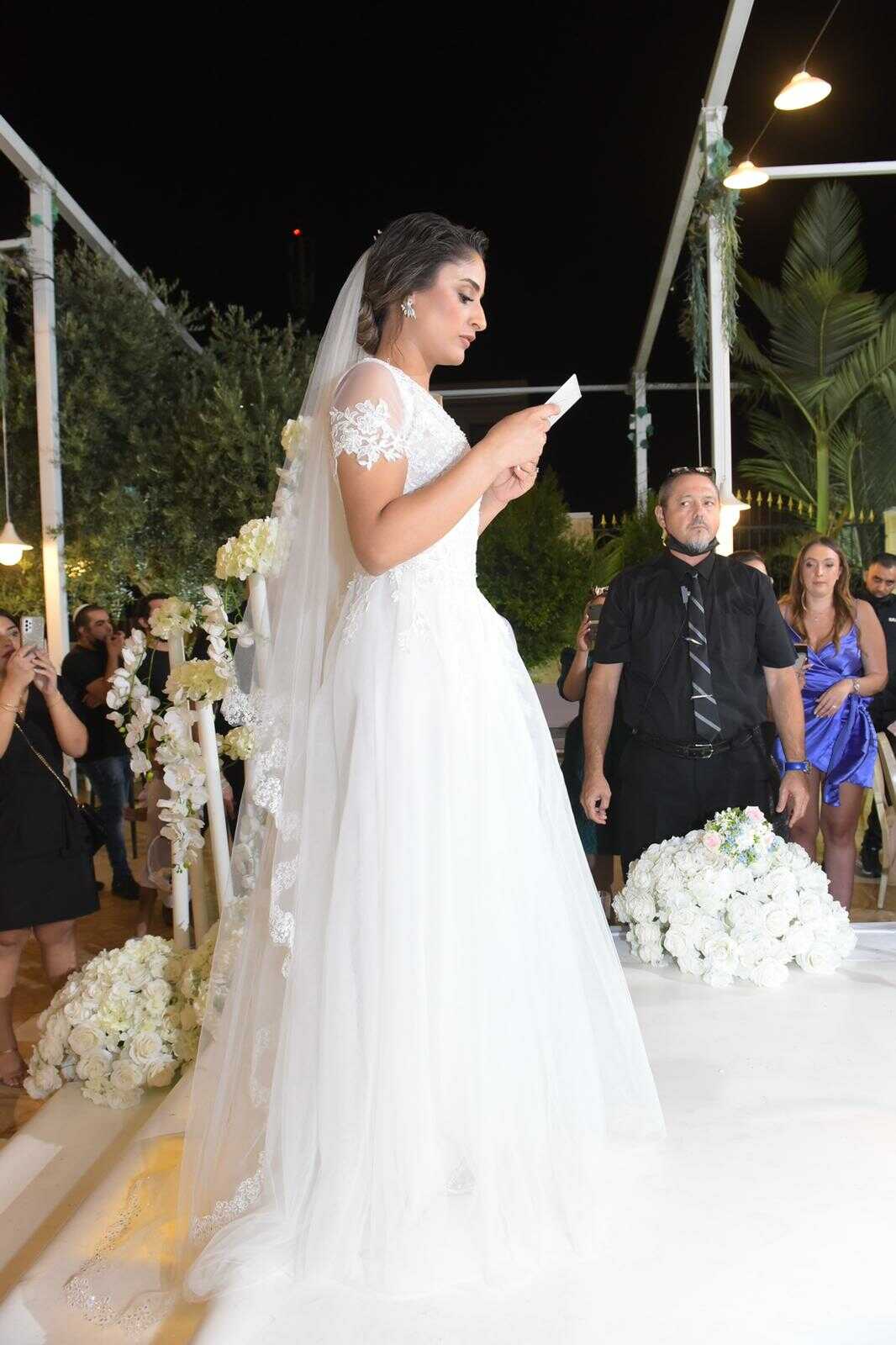 כלה בשמלה לבנה קוראת נדרים בחוץ בלילה. אנשים צופים, חלקם מצלמים.