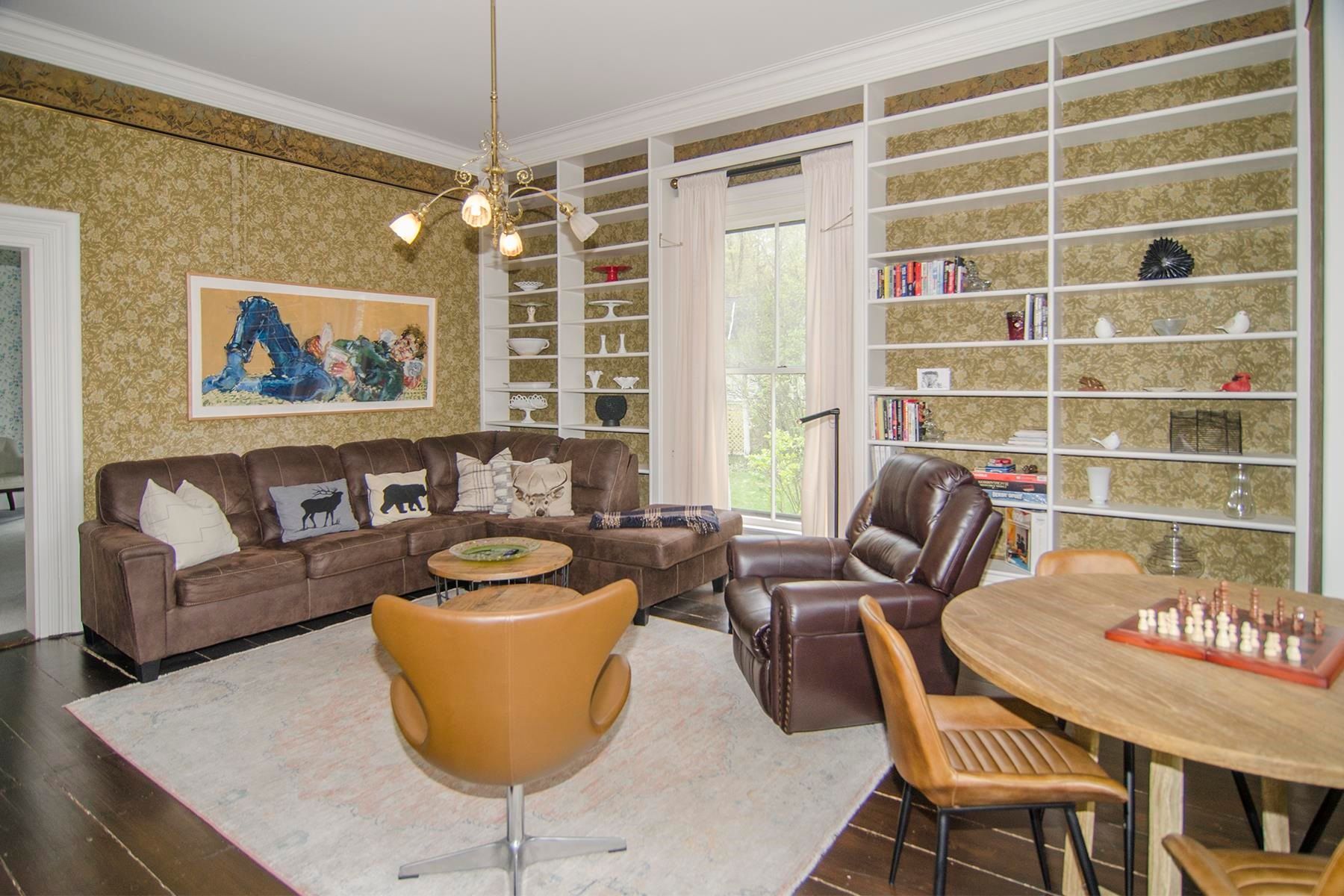 Cozy living room with brown sectional sofa, bookshelves, recliner, round table, rug, and artwork.