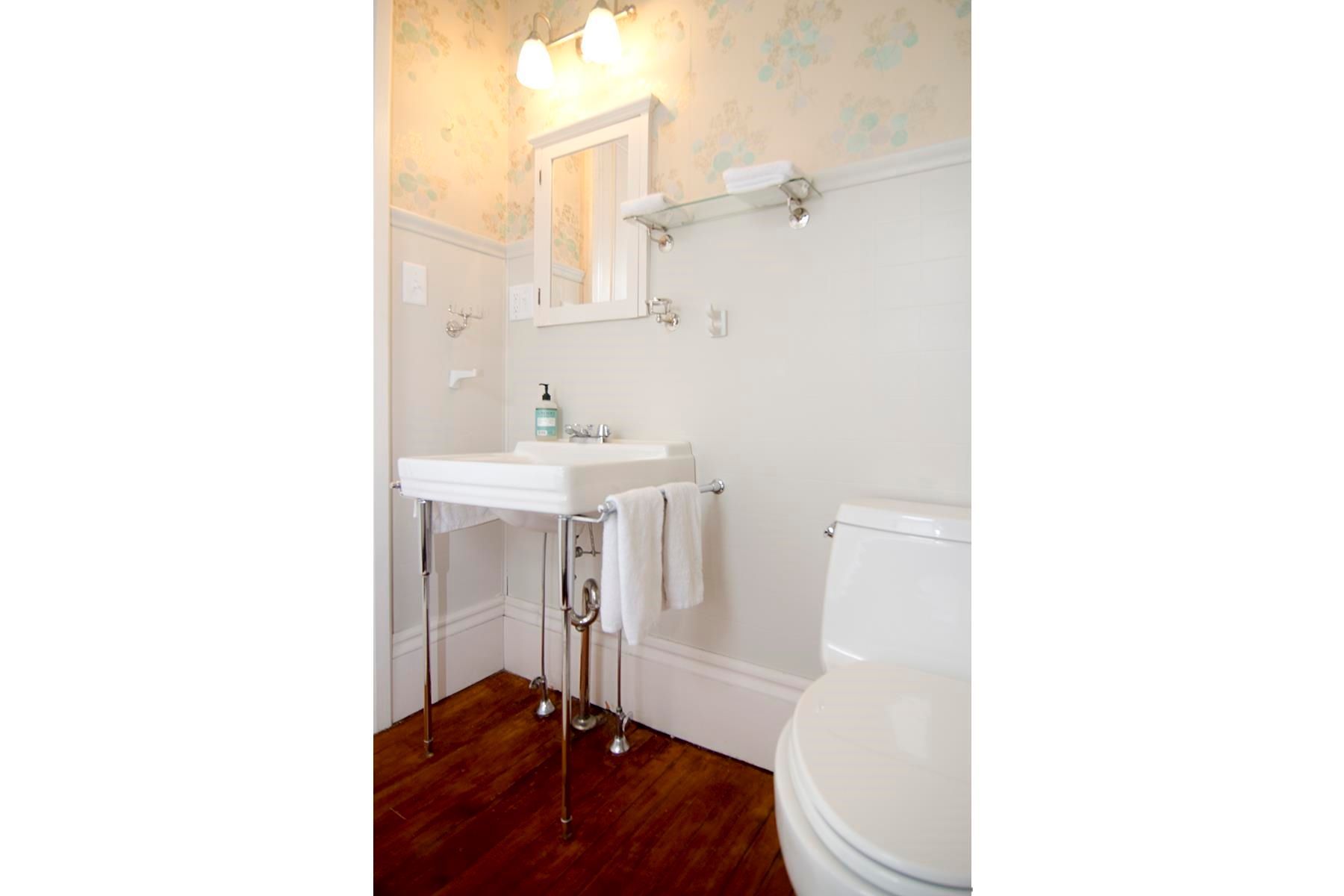 Bathroom with a pedestal sink, white toilet, white walls and dark wood floor.