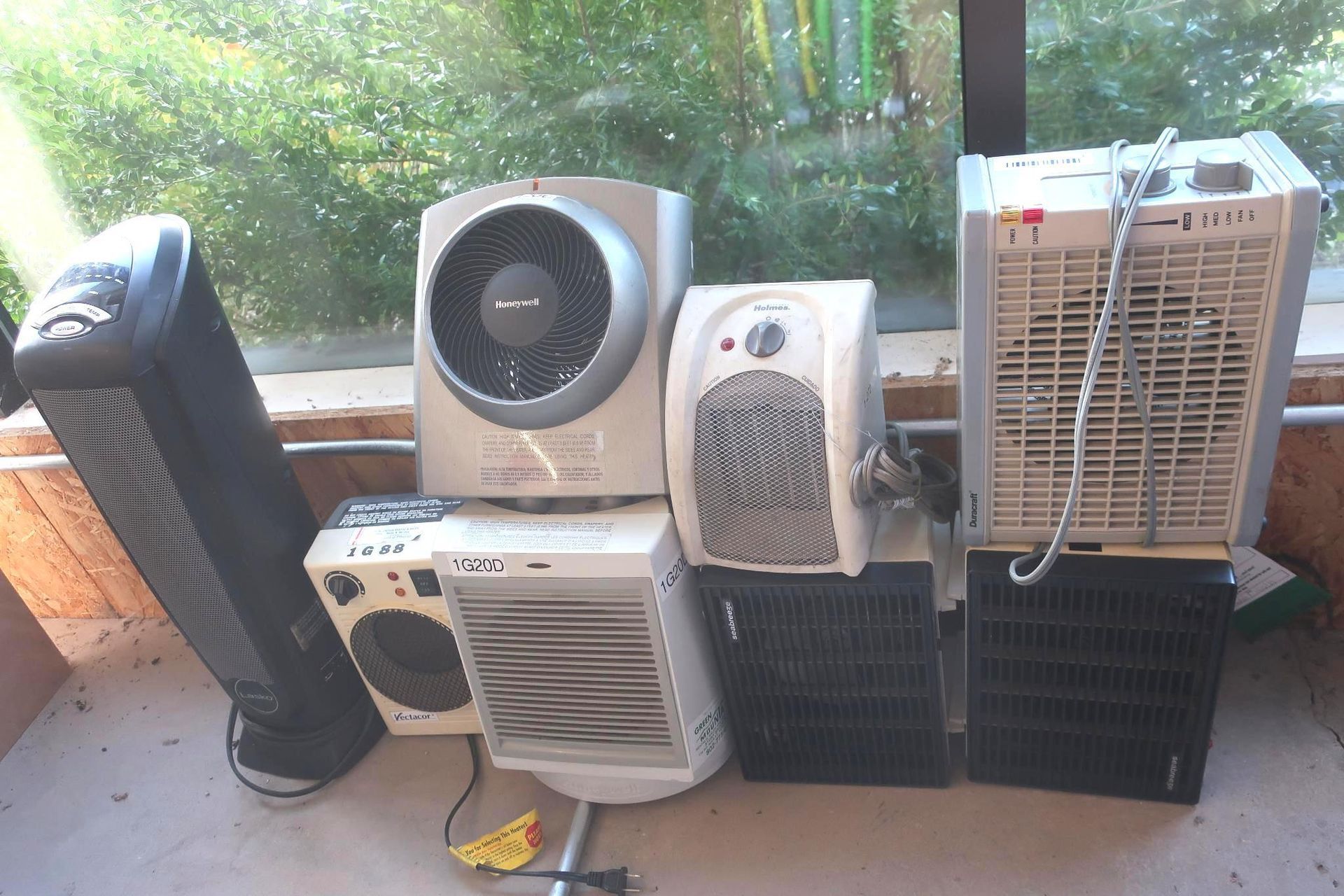 A collection of electric fans and heaters of various shapes and sizes on a patio.