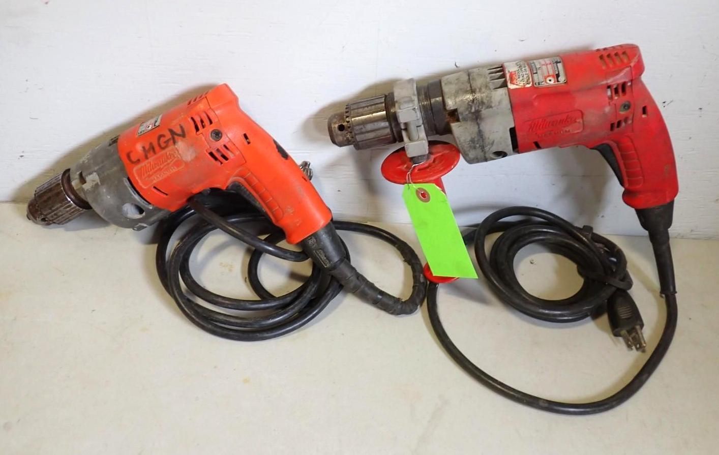 Two corded electric drills, one orange and one red, lying on a white surface with a green auction tag attached.