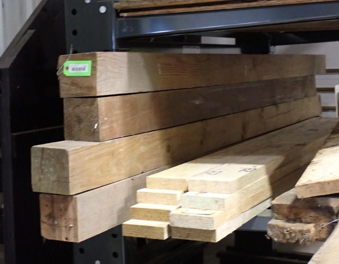 Stacked wooden posts and lumber boards stored on warehouse metal shelving.
