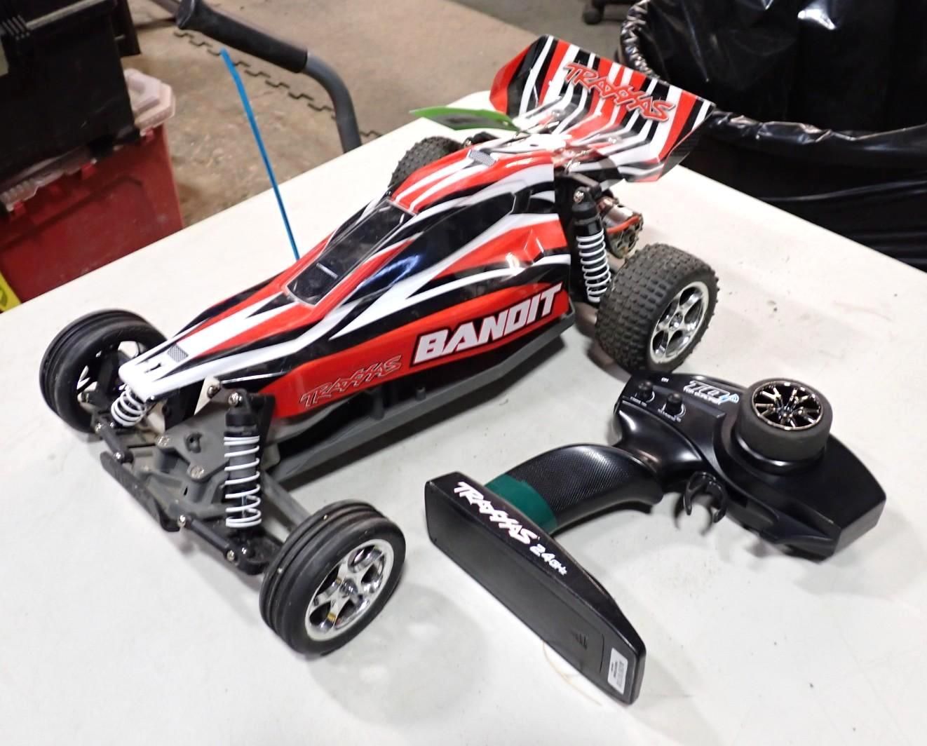 A red, black, and white Traxxas Bandit RC buggy with its remote control on a white surface.