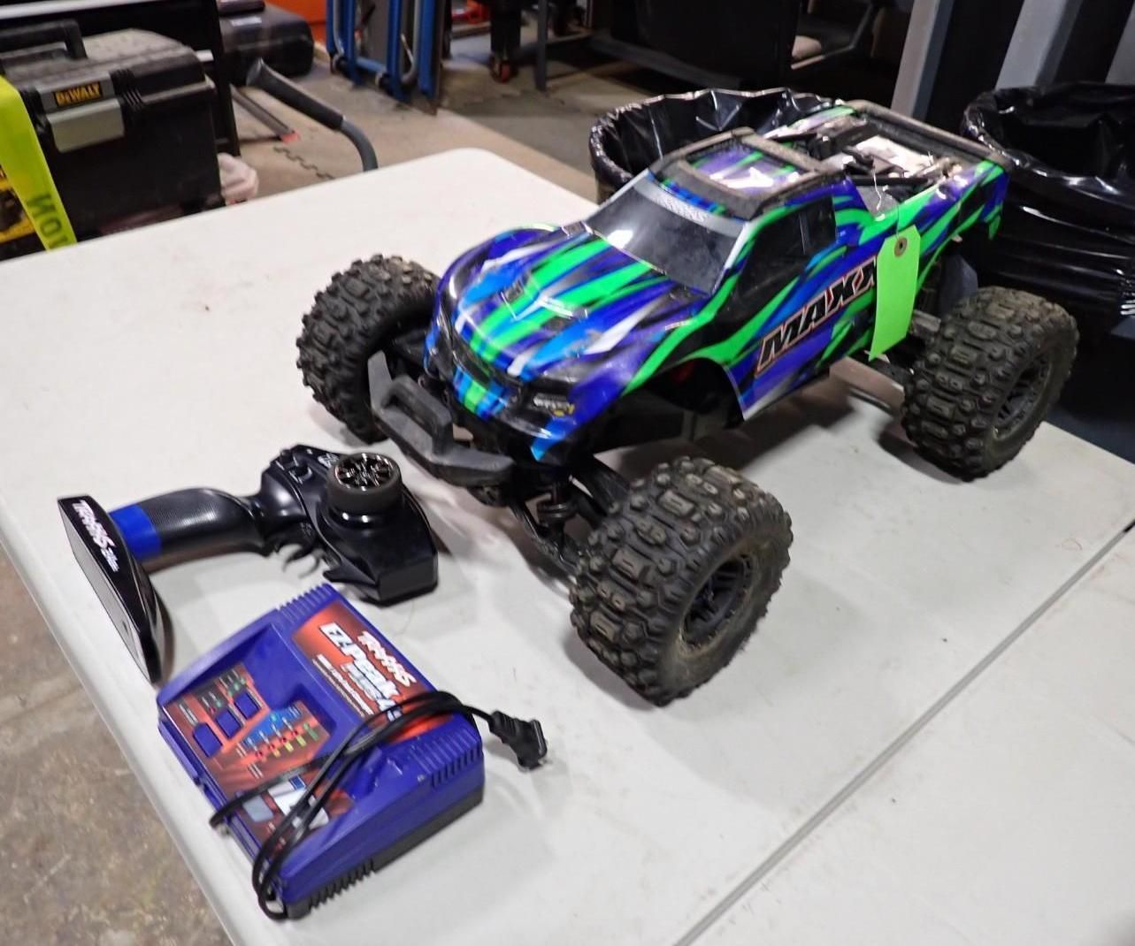 A blue and green remote-controlled Traxxas monster truck with a handheld remote and battery charger on a table.