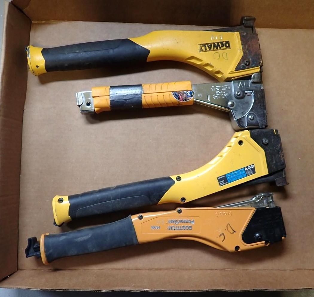 Four hammer tackers with yellow and black handles arranged vertically inside a cardboard box.