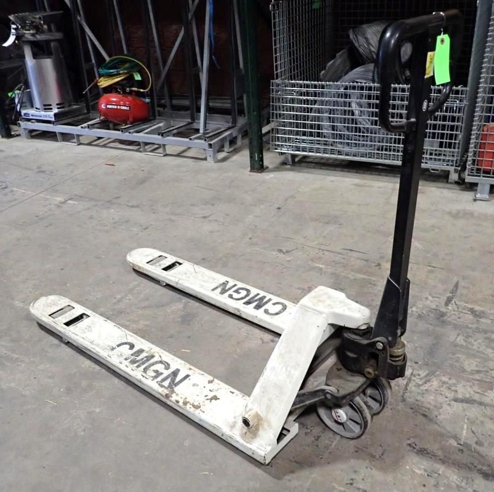 A white CMGN brand manual pallet jack parked on a concrete floor in a warehouse setting.