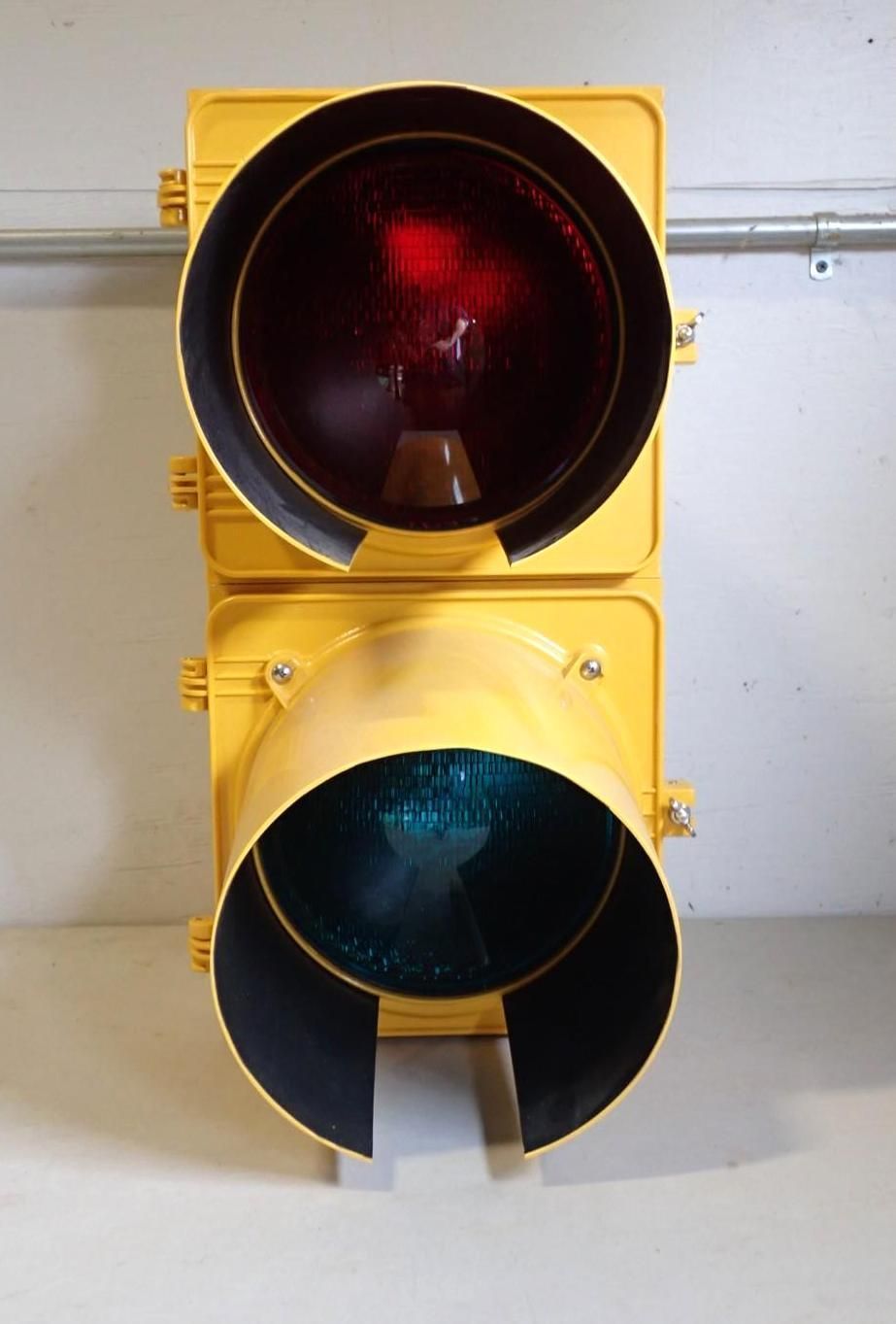 A yellow, two-section traffic light signal with a lit red circular light on top and a dark green signal light below.