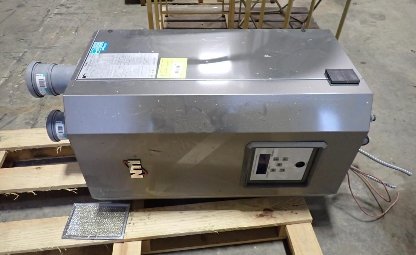 A stainless steel NTI wall-mounted boiler unit sits on a wooden pallet in a workshop.