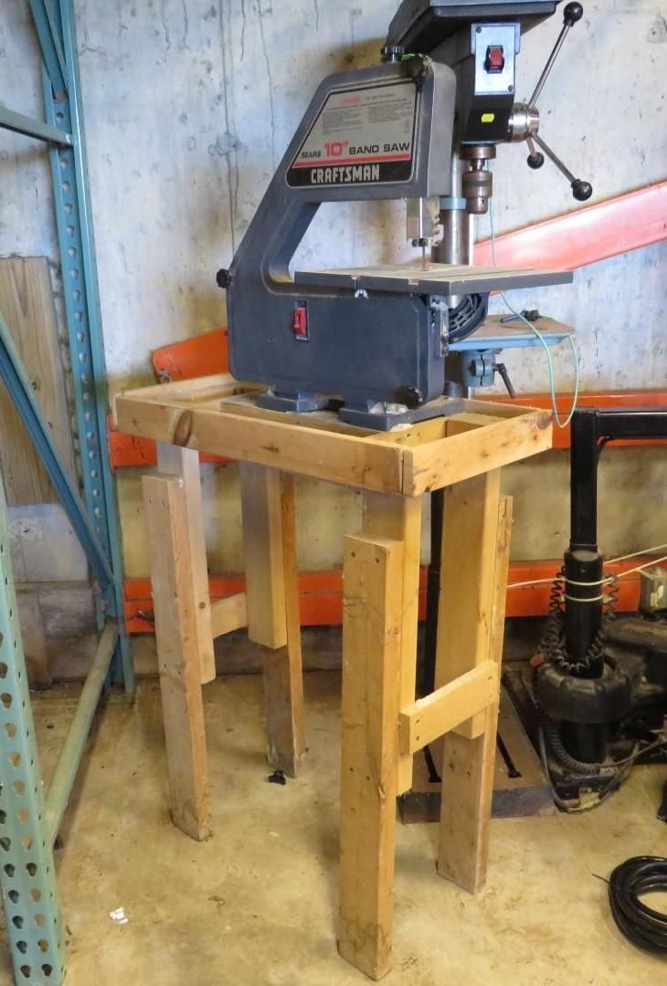 Drill press on a wooden stand in a workshop setting.